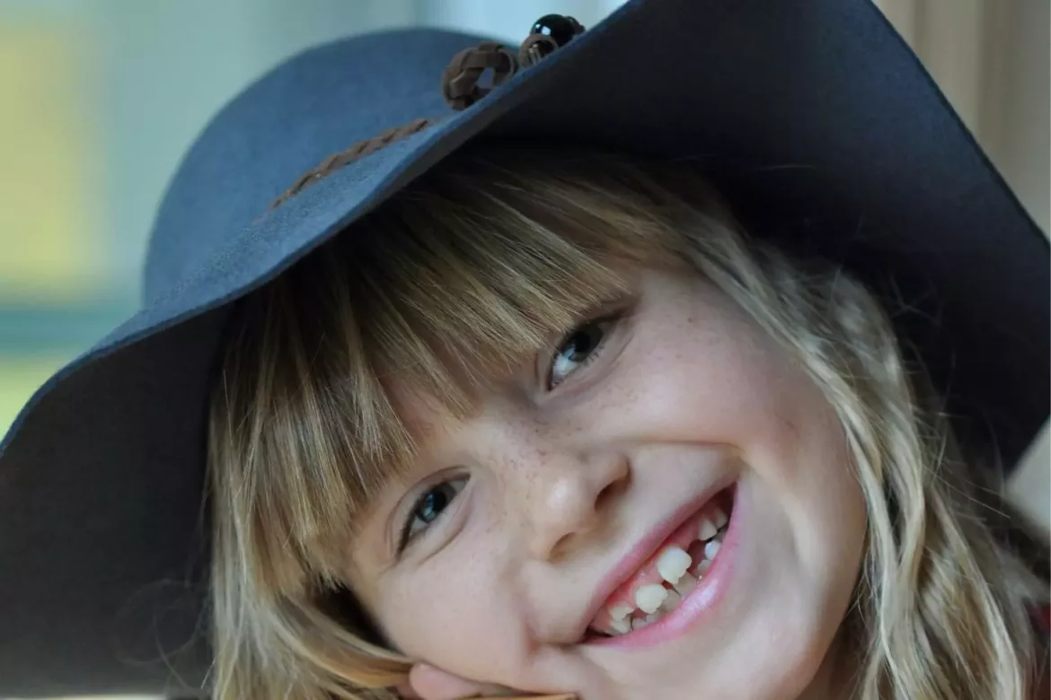Uśmiechnięta dziewczynka w niebieskim kapeluszu po leczeniu w ramach NFZ