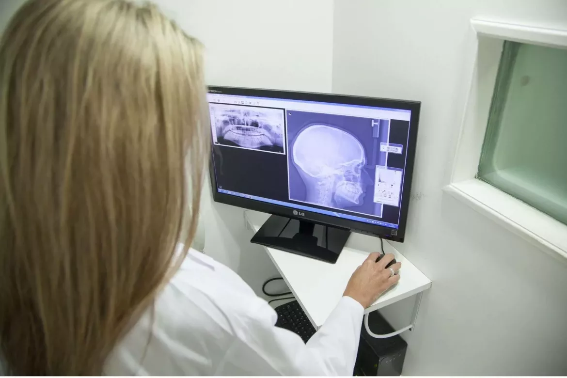 Siedząca tyłem stomatolog na ekranie komputera widzi zdjęcie cefalometryczne pacjenta