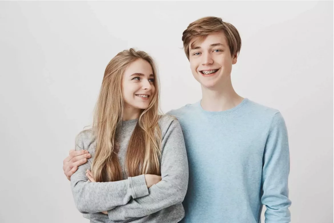 Uśmiechnięci dziewczyna i chłopak z aparatem na zębach stoją na tle białej ściany