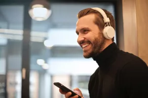 Uśmiechnięty mężczyzna z niewidocznym aparatem na zębach z słychawkami na uszach z telefonem w ręku