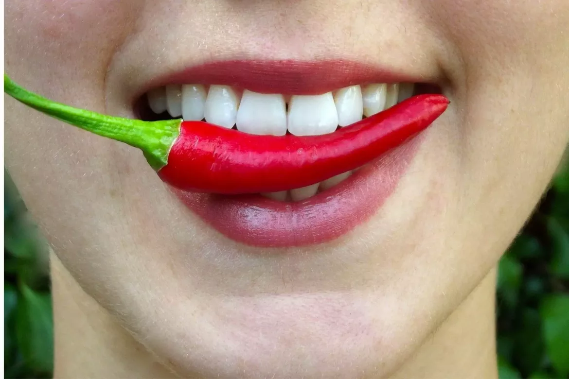 Uśmiechnięta kobieta po wybielaniu zębów trzyma w zębach papryczkę chili